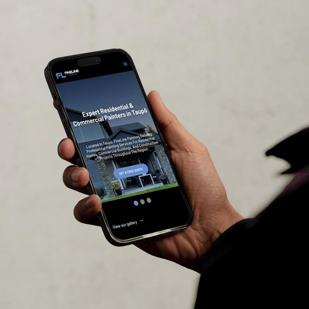 A person holding a smartphone displaying the FineLine Painting website homepage, showcasing a residential house with the headline 'Expert Residential & Commercial Painters in Taupō' and a call-to-action button to get a free quote.