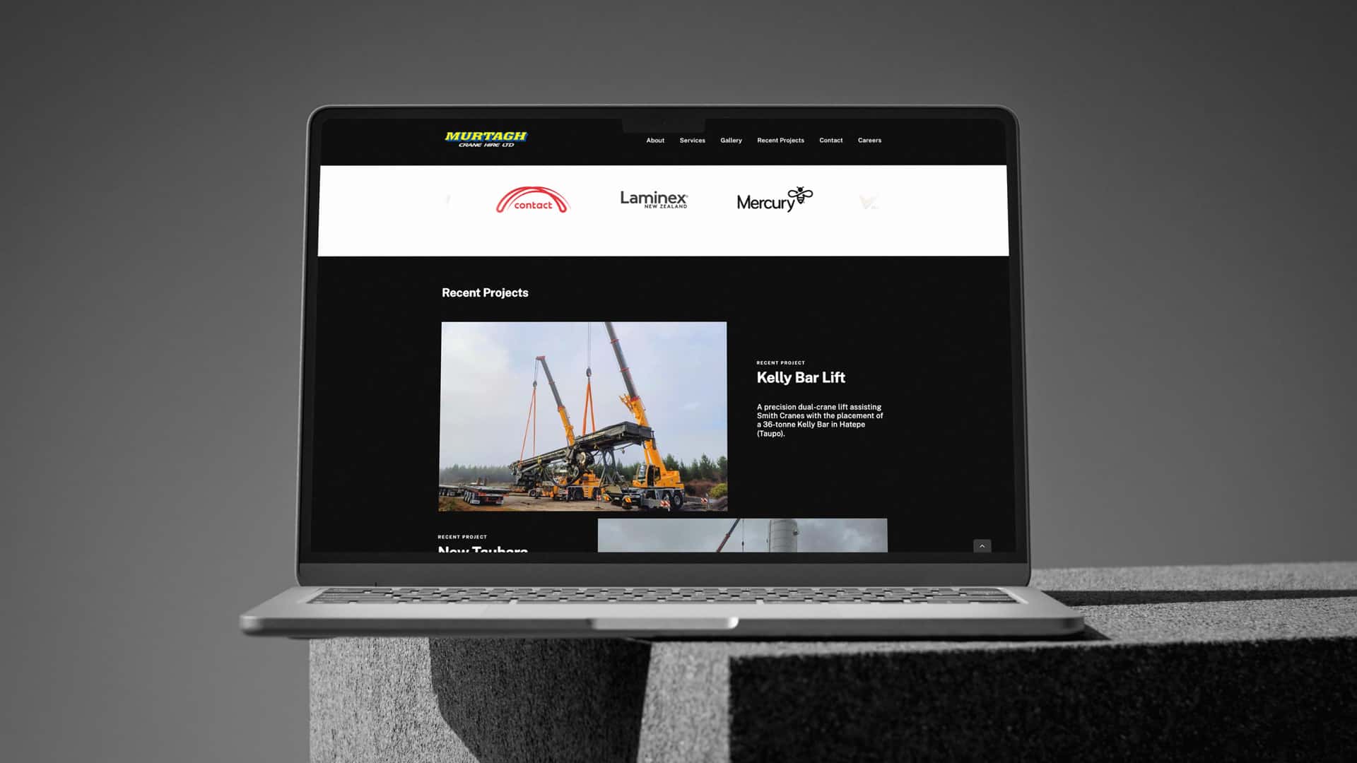 A laptop displaying the Murtagh Crane Hire Ltd website, showcasing the "Recent Projects" section. The highlighted project, titled "Kelly Bar Lift," features a large image of two yellow cranes lifting a massive steel structure, with supporting text describing the precision dual-crane lift for placing a 38-tonne Kelly Bar in Hatepe, Taupō.