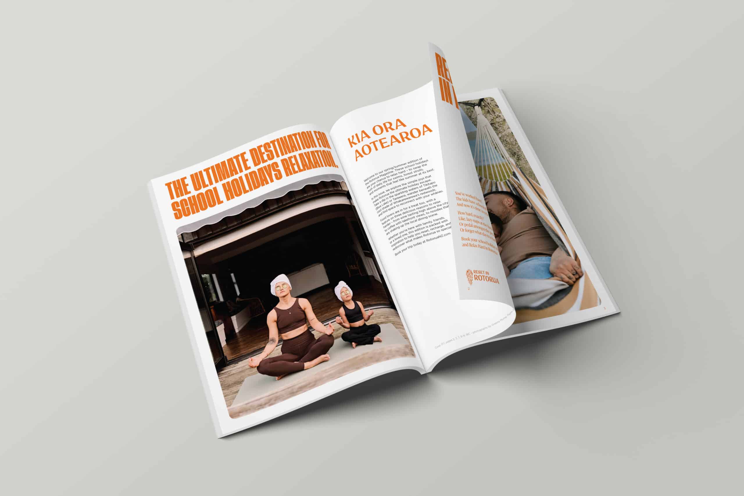 Open magazine on a light grey surface. The left page features a large headline in orange reading 'The Ultimate Destination for School Holidays Relaxation' above a photo of a woman and a child meditating side by side, both wearing towels on their heads. The right page includes the title 'Kia Ora Aotearoa' with body text and a smaller image of a man relaxing in a hammock.