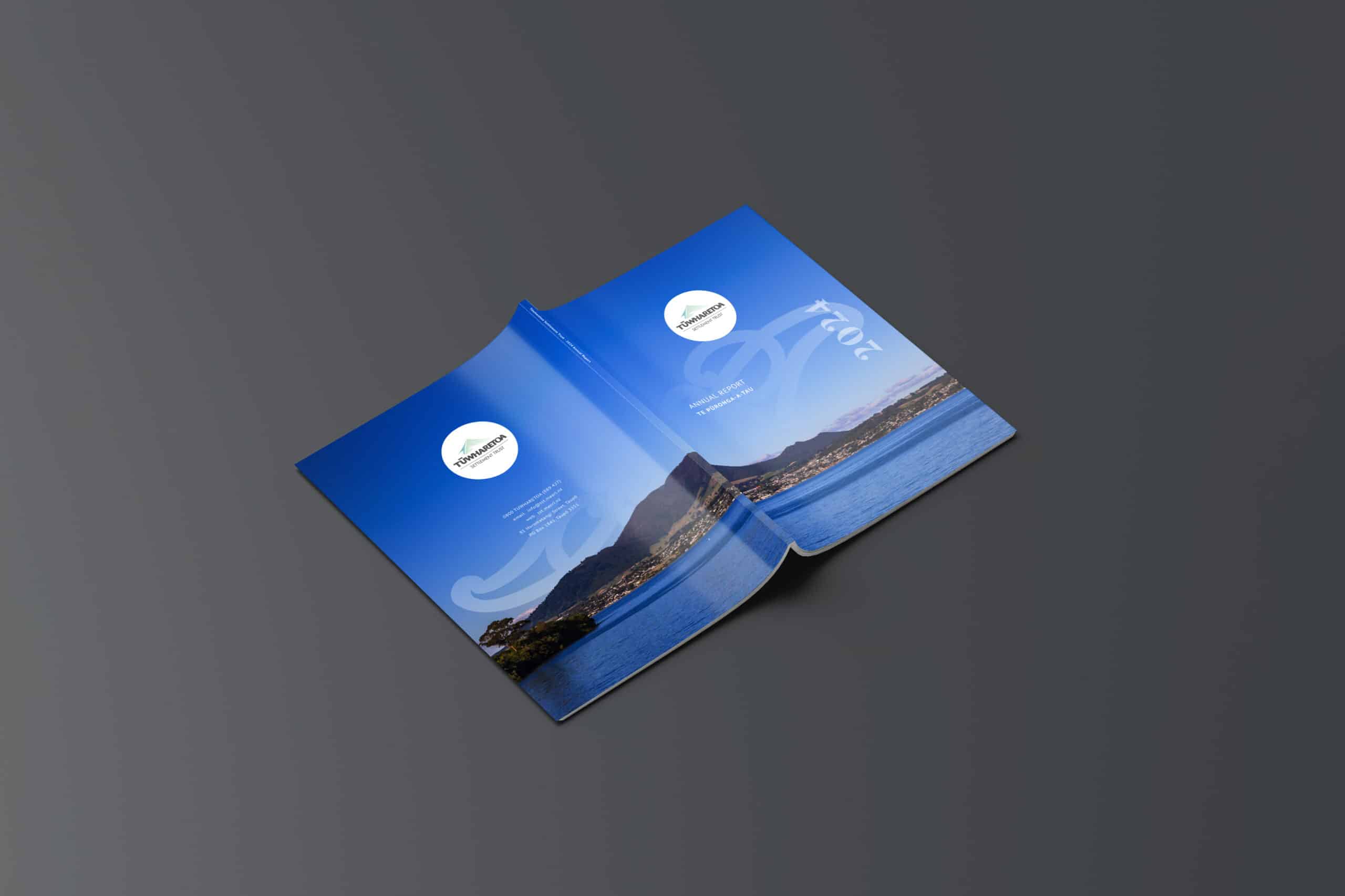 Open annual report laid flat on a dark surface, featuring a scenic cover image of a coastal landscape with mountains in the background, labeled "2024 Annual Report" for Tuwharetoa.